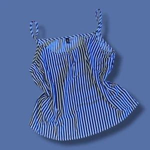 Randig linnetopp - Säljer en snygg randig linnetopp från H&M Divided i vitt och marinblått. Toppen har tunna axelband och en rak, luftig passform som är perfekt för varma dagar. 