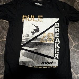 Svart t-shirt med skateboardtryck Firefly 146-152 - Cool svart t-shirt från Firefly med stort tryck framtill i vitt och guld. Motiv med skateboardåkare och texten 'Rule Breaker 28'. Skön passform och tillverkad i mjuk bomull. Perfekt för dig som gillar streetwear och skatevibes.