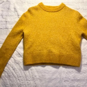 Gul stickad tröja från H&M i mohairmix - Supermysig gul stickad tröja från H&M i mohair- och ullblandning. Tröjan har en croppad passform, ribbade muddar och rund hals. Perfekt för lager-på-lager och ger en färgklick till din outfit.