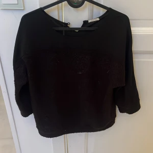Svart blus från Intimissimi med struktur - Svart blus från Intimissimi med snyggt strukturerat tyg framtill och på ärmarna. Blusen har trekvartsärm och rund halsringning med liten knapp i nacken. Perfekt för dig som gillar stilrena och unika detaljer. Skulle uppskatta storleken som storlek s/m!