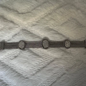 Glittrigt armband med kedjedetaljer - Säljer ett riktigt snyggt armband i silverfärgad metall med flera kedjor och ovala spännen dekorerade med glittrande stenar. Armbandet har en cool och unik design som verkligen sticker ut och passar perfekt om du vill addera lite extra bling till din outfit.