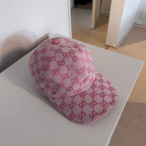 Rosa Gucci keps Dubai - Snygg rosa keps från Gucci med ikoniskt GG-mönster över hela kepsen. Kepsen har böjd skärm, justerbart spänne bak i rosa och är tillverkad i ett slitstarkt bomullsmaterial. Perfekt för dig som vill sticka ut med en lyxig och trendig accessoar.