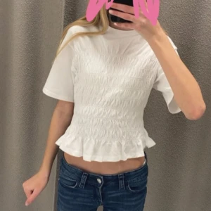 Vit blus med volang från Gina Tricot - Supersöt vit blus från Gina Tricot i storlek XS. Toppen har korta ärmar, smockad midja och en volangkant nertill som ger en feminin och trendig look. Perfekt till jeans eller kjol för en fräsch stil. Passar perfekt nu i sommar , men även i höst och vinter med en kofta till. Jätte bra skick, ny pris runt 300kr. Priset kan diskuteras vid snabbt köp
