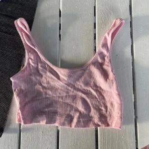 Rosa ribbad linnetopp från H&M Divided - Säljer en ljusrosa croppad linnetopp från H&M Divided. Toppen är ribbad med smala axelband och har en enkel, stilren design som passar perfekt till jeans eller kjol. Supermjuk och skön för varma dagar eller lager på lager.