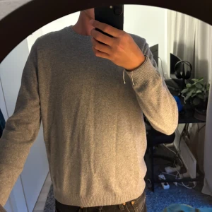 Grå stickad tröja från Oscar Jacobson - Säljer en stilren grå stickad tröja från Oscar Jacobson. Tröjan har rund halsringning, ribbade muddar och är tillverkad i ett mjukt material (30% cashmere 70% wool) som passar perfekt till lager-på-lager.