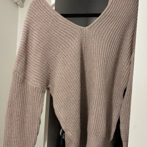 Beige stickad v-ringad tröja - Säljer en beige stickad tröja med v-ringning och lång ärm. Tröjan har en grovstickad struktur och avslappnad passform, perfekt att slänga på sig när det är lite kyligt. Enkel att styla med jeans eller kjol för en chill look.