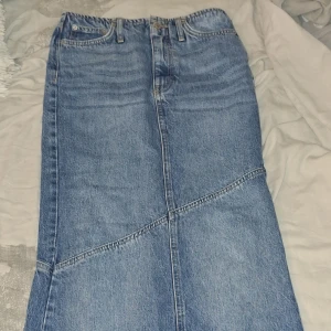 Lång jeanskjol från gina tricot  - Säljer en snygg lång jeanskjol i klassisk blå denim från g perfect jeans. Kjolen har coola snedställda sömmar, femficksmodell och bälteshällor. Perfekt för dig som gillar en avslappnad men trendig stil.