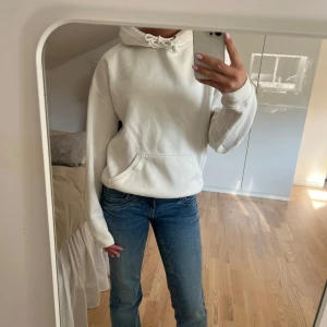 Vit hoodie - Säljer en stilren vit hoodie med huva och snörning. Tröjan har en klassisk känguruficka framtill och långa ärmar med ribbade muddar💗