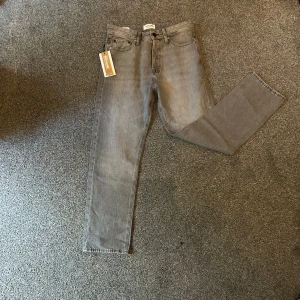 Grå Jack&Jones  jeans - Säljer ett par grå Jack&Jones jeans. Klassisk femficksmodell med läderpatch bak i midjan. Jeansen är i bomull och har en snygg, lite tvättad look. Perfekta för dig som gillar en avslappnad stil.
