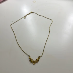 Guldigt halsband med hjärtdetalj - Snyggt halsband i guldton med tunn kedja och ett coolt hänge i form av ett hjärta med vingar. Perfekt accessoar för att lyfta din outfit med en touch av romantisk och edgy stil.