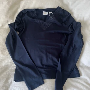 Mörkblå långärmad topp med spets Gina Tricot - Supersnygg mörkblå långärmad topp från Gina Tricot med v-ringning och fina spetsdetaljer vid halsen. Tillverkad i mjuk bomullsmix som känns skön mot huden. aldrig kommit till användning pga för kort och gillar inte passformen 💙