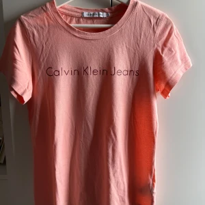 Rosa t-shirt från Calvin Klein Jeans - •Snygg rosa t-shirt från Calvin Klein Jeans med enkel och clean design.  •Använd 2 gånger, är som ny. Tvättad. •T-shirten har rund halsringning, korta ärmar och tryckt logga framtill.  •Tillverkad i mjuk bomull som känns skön mot huden.  •Perfekt för en chill och stilren look. •Djurfritt och rökfritt hem.