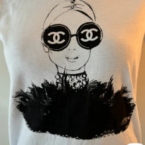 Vit t-shirt med svart konstnärligt tryck - Vit t-shirt med ett stort svart grafiskt tryck framtill. Klassisk passform och rund halsringning. Perfekt för dig som gillar unika och kreativa motiv.