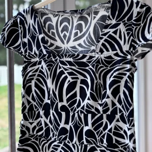 Svartvit kortklänning med otroligt vackert mönster - Kortklänning i svart och vitt med ett unikt grafiskt mönster. Klänningen har korta ärmar och en lätt utställd kjol. Sval och skön, perfekt för varma dagar. Materialet känns som bomull och passformen är normal. Snygg v-ringning framtill. Den har dragkedja på kedjan.