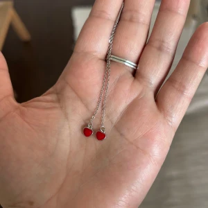 Silverörhänge  med röda hjärtan - Säljer ett par tunna silverörhängen 925  med kedja och små röda hjärtan längst ner. Hjärtana är blanka och ger en söt detalj till looken. Perfekta för dig som gillar minimalistiska smycken med en pop av färg. ( jag glömde vad köpte men tror är från L8Hasselblad )