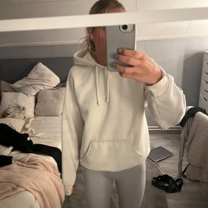 Vit hoodie med huva och ficka - Säljer en enkel och stilren vit hoodie med huva och dragsnören. Tröjan har en stor magficka och långa ärmar med breda muddar. Perfekt för chill dagar eller när du vill ha något bekvämt och snyggt.