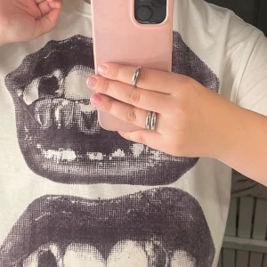 Vit t-shirt med grafiskt tryck - Vit t-shirt med ett stort, grafiskt tryck av två svarta munnar med tänder på framsidan. Klassisk rund hals och korta ärmar. Materialet känns som bomull och passformen är normal. 