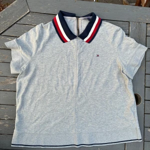 Grå polotopp Tommy Hilfiger XXL - Snygg grå polotopp från Tommy Hilfiger i storlek XXL. Tjock krage i marinblått, rött och vitt med dragkedja bak. Kortärmad modell med liten logga på bröstet och diskret mörkblå kant nertill.