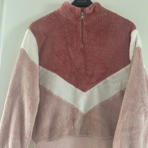 Rosa fleece-tröja från H&M Divided XS - Supermjuk fleece-tröja i rosa och vitt från H&M Divided. Tröjan har halv dragkedja, lång ärm och coolt V-format mönster framtill. Perfekt för dig som gillar mysiga och trendiga plagg med lite oversized känsla.