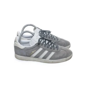 Grå Adidas Gazelle sneakers - Snygga Adidas Gazelle sneakers i grå mocka med vita detaljer och klassiska tre ränder på sidan. Tecken på användning finns men dem är fortfarande i väldigt bra skick, inga skador förutom att dem är lite smutsiga men det går att tvätta bort❤️