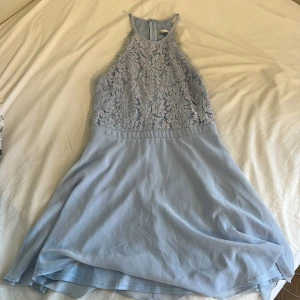 Ljusblå spetsklänning från NLY Trend - Supersöt ljusblå kortklänning från NLY Trend med blommig spets upptill och flowy kjol. Hög halsringning och dragkedja bak. Perfekt för dig som vill ha en feminin och fräsch look till sommaren!