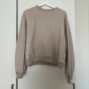 Beige sweatshirt från Nelly - Beige sweatshirt från Nelly i storlek S. Tröjan har en loose passform, ribbade muddar vid ärmslut och nederkant samt rund halsringning. Mjuk insida i fleece för extra komfort. Perfekt för en chill och avslappnad stil.