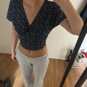 Blommig croppad blus med v-ringning - Söt croppad blus i mörkblått med små vita blommor. Toppen har korta ärmar och en djup v-ringning framtill. Passar även M/38. 