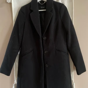 Svart kappa från Vero Moda XS - Stilren svart kappa från Vero Moda i klassisk modell med tre knappar framtill och diskreta fickor. Jackan har lång ärm, snygg krage och är tillverkad i ett ullblandat material som passar perfekt för kyliga dagar.