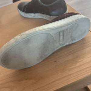 Svarta sneakers i sammet från Lanvin - Snygga svarta sneakers från lanvin med ovandel i sammet och tåparti i blankt material. Skorna har svarta snören och en vit, något chunky sula. Perfekta för dig som gillar en stilren men ändå unik look.