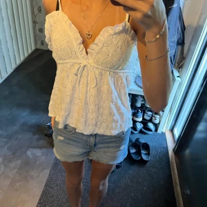 Vit sommar topp - Superfin vit linnetopp med smala axelband, broderade blommor och volangdetaljer vid ringningen. Toppen har v-ringning och knyt framtill för en söt och somrig look. Perfekt till shorts eller kjol när det är varmt ute! Säljer då jag har två likadana 
