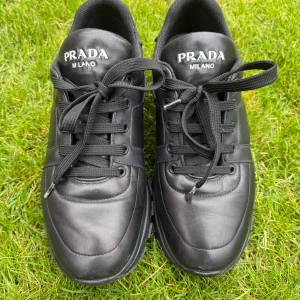Svarta sneakers från Prada Milano str 42  - Snygga svarta sneakers från Prada Milano i skinn med robust sula och klassisk snörning. Skorna har en stilren design med rund tå och diskreta sömmar. Perfekta för dig som gillar exklusiva och tidlösa sneakers med premiumkänsla.