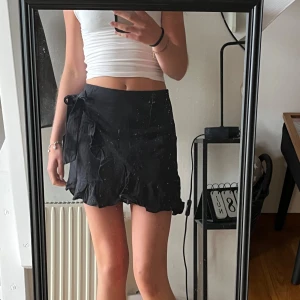 Svart omlottkjol med volang - Supersöt svart  omlottkjol med volangkant och knyt i sidan. Tyget påminner om linne och är inte alls genomskinligt. Enkel att styla och passar  perfekt till crop tops eller stickade tröjor💕