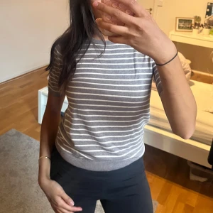 Gråvit randig kortärmad tröja - Superfin grå tröja med vita horisontella ränder och korta ärmar. Tröjan har rund halsringning och ribbade kanter vid ärmslut och nederkant. Perfekt för dig som gillar en enkel men stilren look.