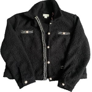 Svara jacka från Holy&Whyte  - Svart teddyjacka från Holly & Whyte i storlek L. Jackan har pärlknappar, dekorativa fickor med vita detaljer och en krage.                                         Materialet är mjukt och fluffigt.