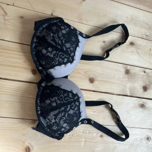Svart spets-bh med detaljer, 70C - Snygg bh i svart spets med blommigt mönster och vadderade kupor i ljusgrått. Axelbanden är justerbara och har silvriga ringdetaljer. Perfekt för dig som gillar en feminin och trendig look.