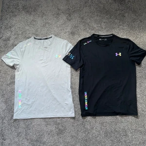 Under Armour tränings-tshirts svart & grå - Två snygga Under Armour t-shirts i svart och ljusgrått. Båda har kort ärm, rund hals och färgglada loggor samt tryck på bröst, ärm och nederkant. Perfekta för träning med lätt och snabbtorkande material som andas. Stilren design med sportig vibe. En tröja för 400kr två för 700kr