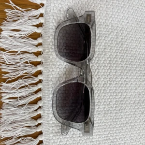  solglasögon CHIMI  - Snygga solglasögon från CHIMI i modellen CORE 04 med transparent grå båge och mörka glas. Rektangulär form och stilren design, perfekt för dig som vill ha en modern vibe. Bågarna är i plast och har diskreta CHIMI-detaljer på sidorna.