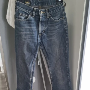 Blå raka jeans från Lee - Klassiska blå jeans från Lee med raka ben och snyggt slitna detaljer. Jeansen har fem fickor, gylf med dragkedja och Lee-logga på knappen. Perfekta för dig som gillar en tidlös och avslappnad look.