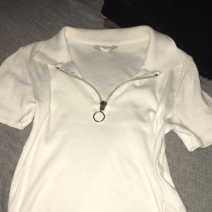 Vit ribbad pikétröja från Topshop - Vit ribbad pikétröja från Topshop med korta ärmar och en snygg half zip-dragkedja med ringdetalj. Tröjan har klassisk krage , perfekt för en clean och fräsch look.