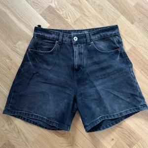 Svarta jeansshorts från Amisu - Snygga svarta jeansshorts från Amisu DNM Collection i klassisk femficksmodell. Shortsen har en rak passform, knapp- och dragkedjestängning samt bälteshällor. Perfekta för en chill sommarlook med en vintage vibe. Har en defekt på baksidan. 