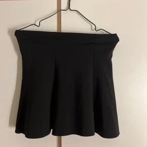 Svart kortkjol från Lindex Kids - Enkel och stilren svart kortkjol från Lindex Kids. Kjolen har en lätt utsvängd form och stängs med dragkedja i sidan. Perfekt för dig som gillar en klassisk look och vill ha något som funkar till många olika outfits.