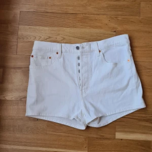 Vita Levi's 501 jeansshorts  - Snygga vita jeansshorts från Levi's modell 501 med klassisk femficksdesign och knappgylf. Shortsen har Levi's ikoniska läderpatch bak och är tillverkade i kraftig bomull. Perfekta för sommar eller semester. 