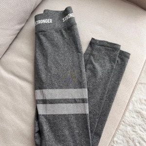 Stronger träningsbyxor - Snygga grå leggings från Stronger med vita ränder på benen och logga i midjan. 