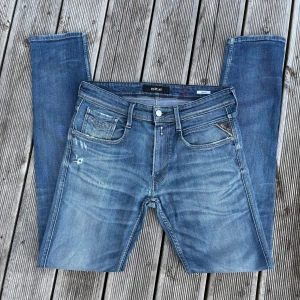 Replay Anbass blå jeans herr - Säljer ett par Replay Anbass jeans i klassisk blå tvätt med snygga slitningar och detaljer. Jeansen har fem fickor, dragkedjegylf och Replay-logga på bakfickan. Slim passform och stilren look, perfekta till sneakers. Kom gärna med frågor🙌 