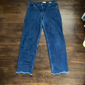 Blå wide jeans från Zara med rå kant - Säljer ett par blå jeans från Zara i storlek 42. Modellen är wide fit med mid waist och rå, fransig kant nertill.