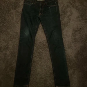 Mörkblå jeans från Nudie Jeans - Snygga mörkblå jeans från Nudie Jeans. Klassisk femficksdesign med orangea kontrastsömmar och broderad bakficka. Tillverkade i slitstarkt jeansmaterial, perfekta för en clean och stilren look.