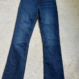 Mörkblå bootcut jeans från Wrangler - Snygga mörkblå jeans från Wrangler med klassisk femficksdesign och bootcut-ben. Jeansen har en normal passform och är tillverkade i mjukt denimtyg med läderpatch bak i midjan. Perfekta för dig som gillar en tidlös och avslappnad look.