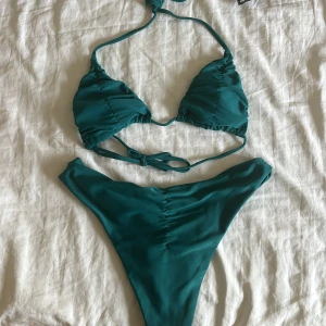 Turkos bikini med snörning från prettylittlething  - Snygg turkos bikini från H&M med trekantsbikinitopp och knyt i nacken och ryggen. Underdelen har hög midja och rynkade detaljer framtill. Perfekt för stranden eller poolen, enkel men trendig design.