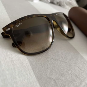 Ray-Ban solglasögon brunmelerad - Snygga Ray-Ban solglasögon med brunmelerad båge och stora fyrkantiga glas. Glasen är tonade i brunt och bågen har klassisk Ray-Ban-logga på sidan. Kommer med originalfodral i brunt läder. Perfekt accessoar för en cool look.