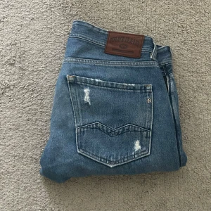 Replay jeans  - Säljer ett par klassiska blå jeans från Replay, modell ROC CO. Jeansen har raka ben, normal passform och snygga slitningar på fickor och lår. Tillverkade i bomull med traditionell femficksdesign och läderpatch bak i midjan. Längd 106 cm.